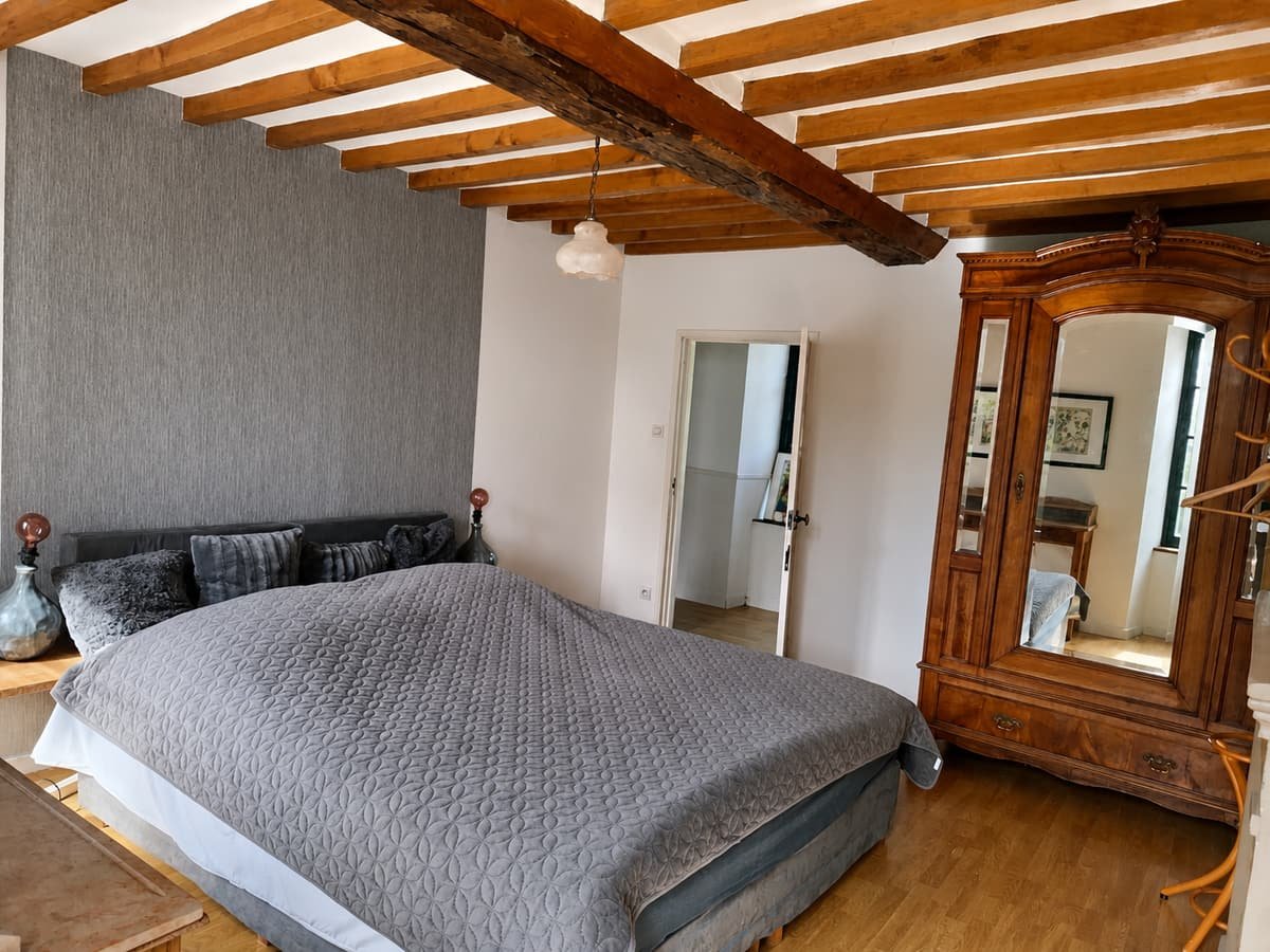 Slaapkamer met tweepersoonsbed, houten balkenplafond en een antieke spiegelkast