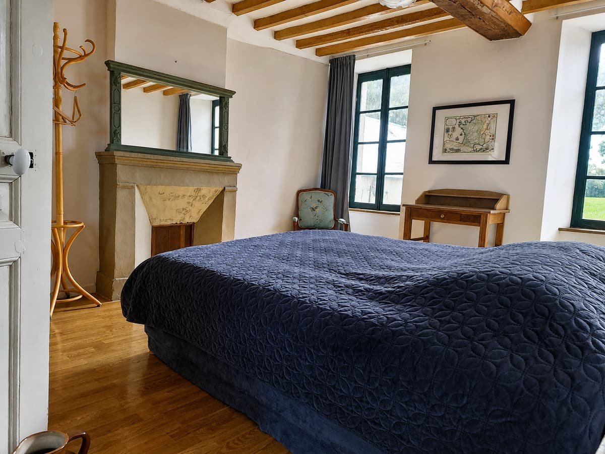 Slaapkamer met donkerblauw beddengoed en een stenen schouw tegen de muur