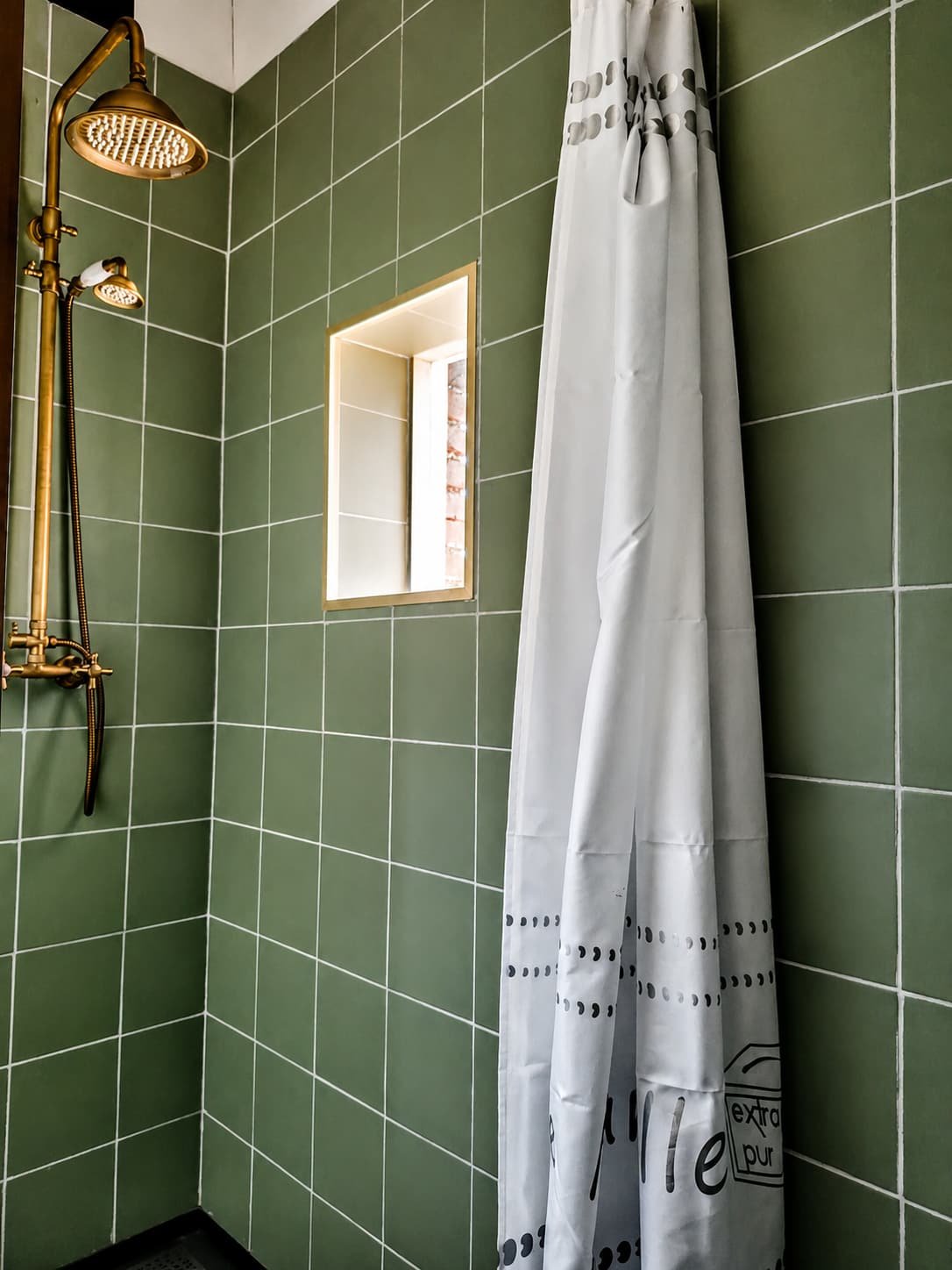 Badkamer met saliegroene tegels en een douche bij het raam