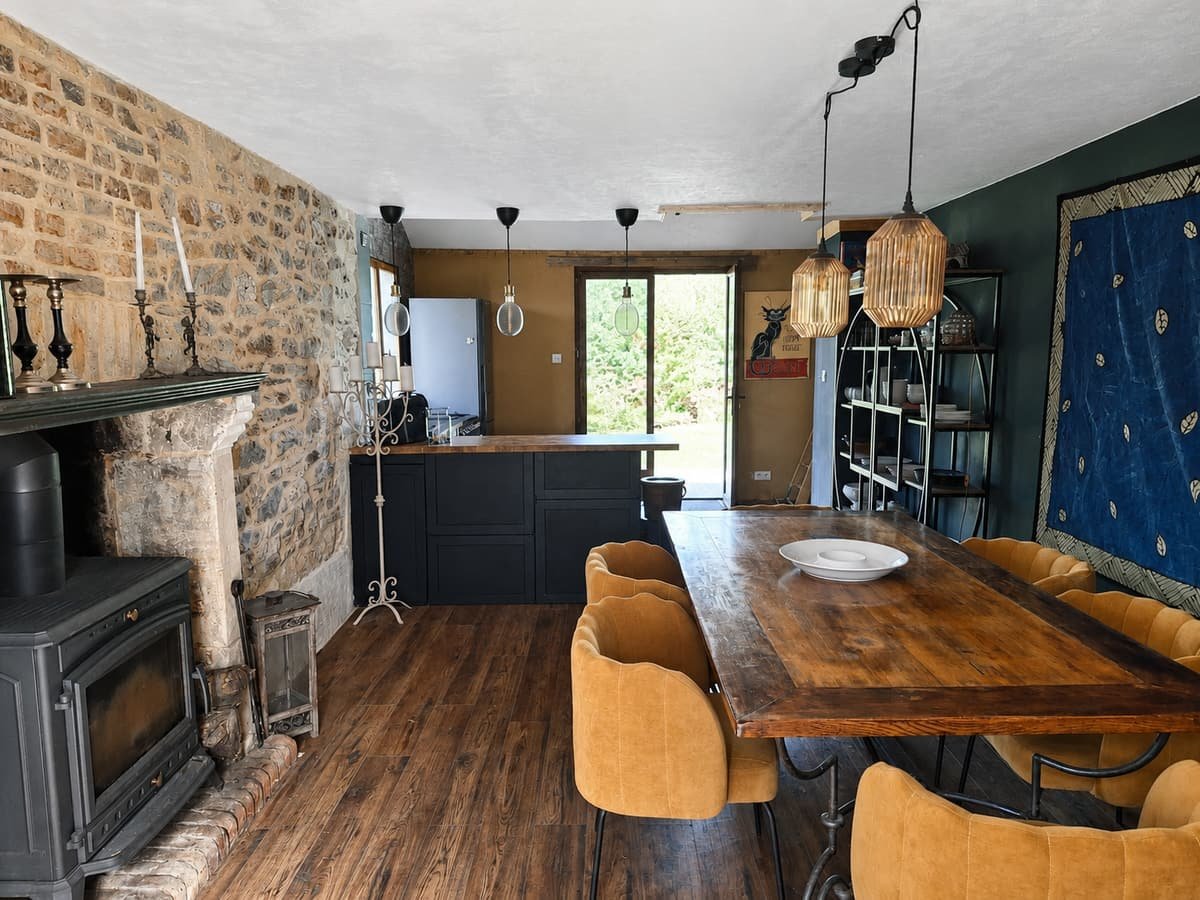 Eettafel met okergele stoelen voor een natuurstenen muur en houtkachel