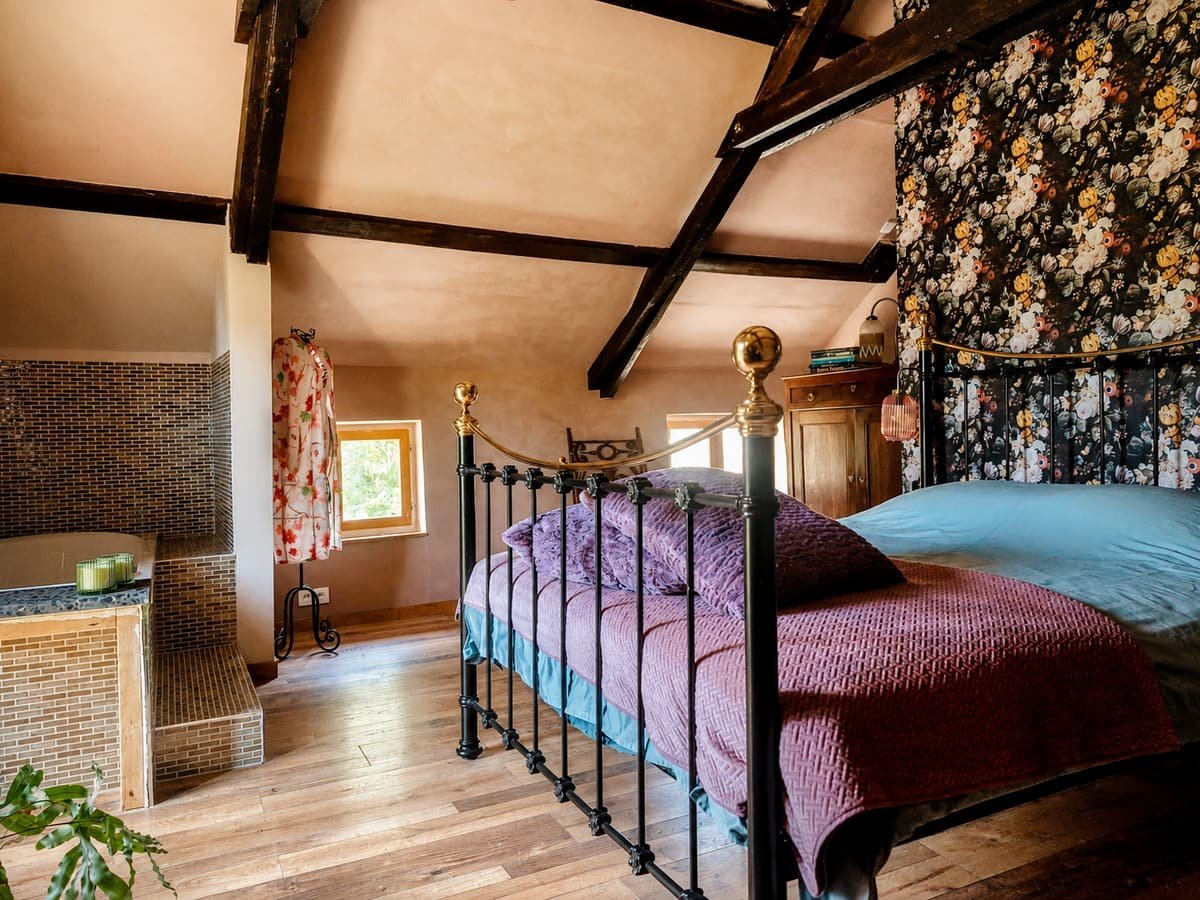 Zolderkamer met smeedijzeren bed, bloemenbehang en zichtbare dakspanten