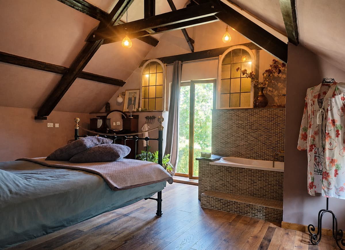 Slaapkamer met vrijstaand bad naast het bed en boogramen naar de tuin