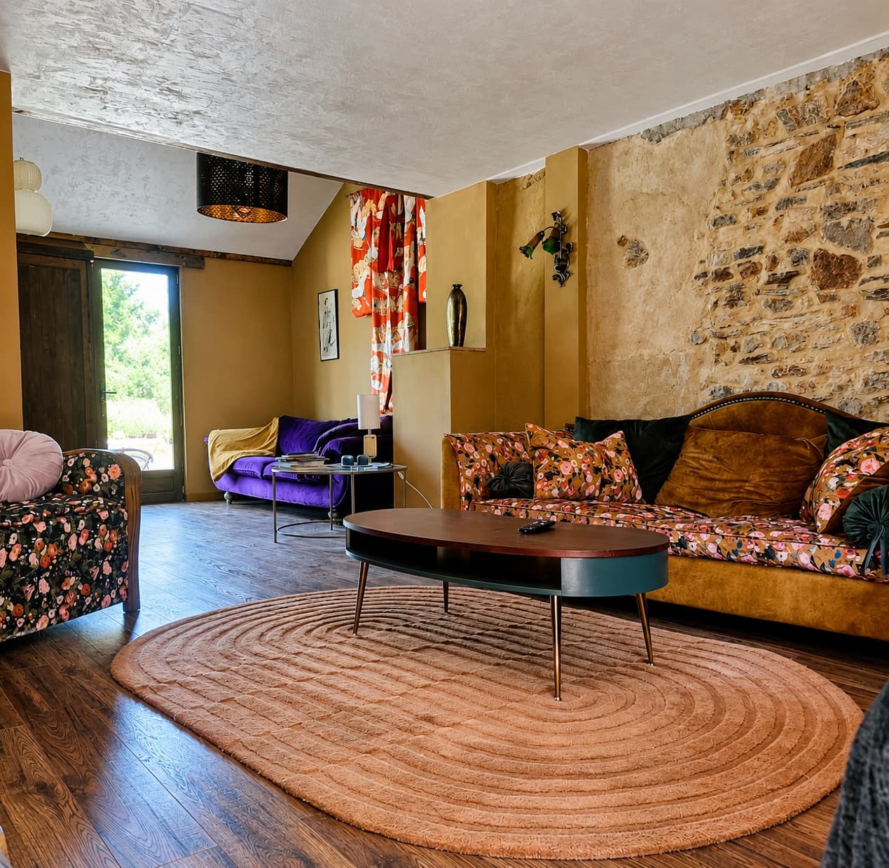 Woonkamer met okerkleurige bank, bloemenstoelen en een natuurstenen muur